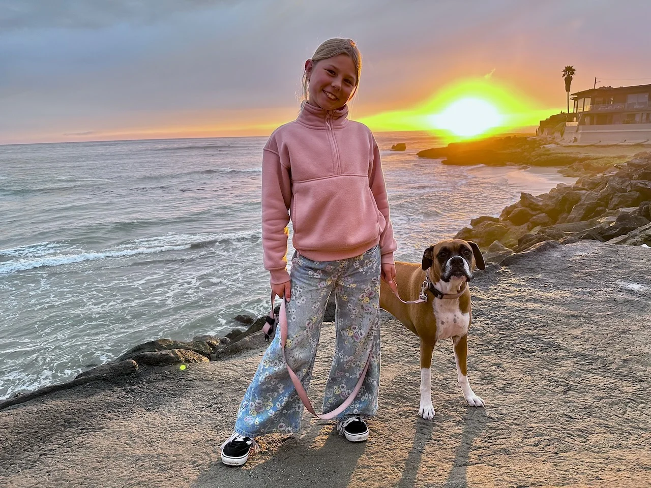 Ivy standing with a boxer beside the ocean at sunset in Pleasure Point